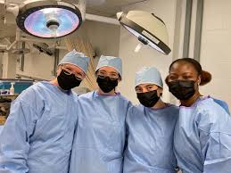 Four doctors pose together in an operating room wearing scrubs and masks.