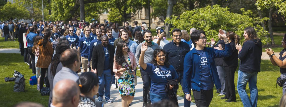 CWRU students smiling and waving as they walk through the quad